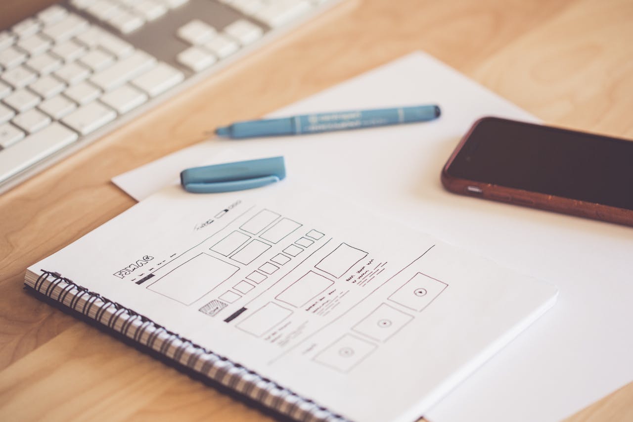 class-01 A neat workspace featuring a sketchpad with wireframes, a smartphone, and a keyboard on a wooden desk.